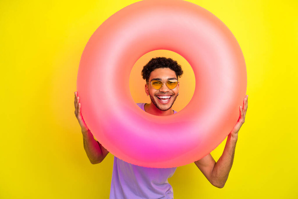 Photo of excited cheerful person look through inflatable ring hole have good mood isolated on yellow color background. - Photo, Image