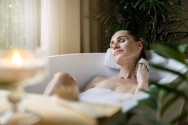 woman enjoying spa bath with foam and body massage brush - Фото, изображение