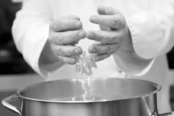 foto en blanco y negro del chef poniendo fideos en la olla en la cocina, primer plano - Foto, Imagen