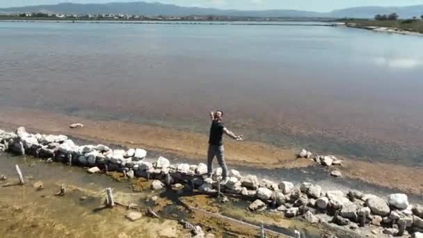 Hombre de pelo oscuro camina a lo largo de una franja de tierra que divide dos estanques - Metraje, vídeo