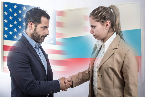 Mann und Frau schütteln sich angespannt die Hände und im Hintergrund die Flaggen Amerikas und Russlands - Foto, Bild