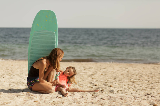 Moeder in een badpak samen met haar dochter veel plezier op een strand aan zee. - Foto, afbeelding