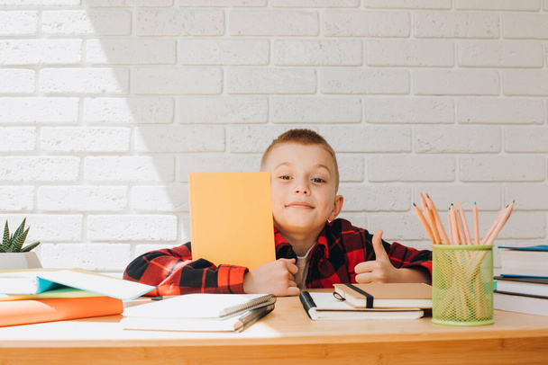 コンセプトは学校に戻ります。勉強中の男の子は本、ノート、鉛筆でテーブルに座っています。正面図 - 写真・画像