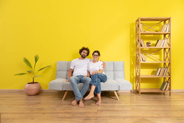 moving, home and couple concept - smiling couple relaxing on sofa in new home. Family - Fotó, kép