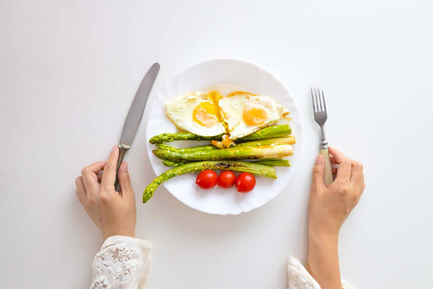 Femme mangeant des œufs frits avec des asperges pour le petit déjeuner. Petit déjeuner sain. - Photo, image