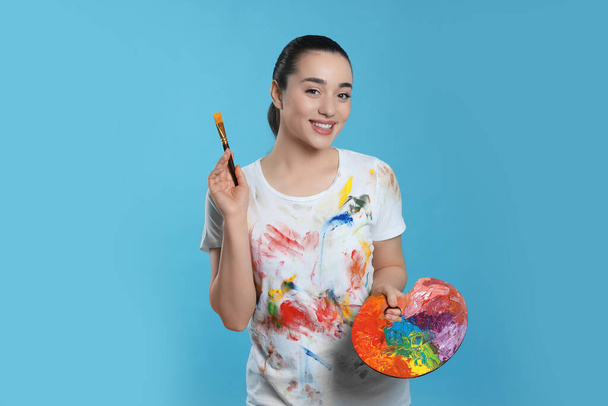Woman with painting tools on light blue background. Young artist - Foto, Imagem