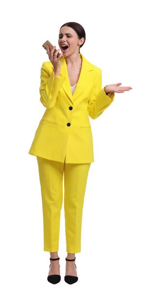 Beautiful emotional businesswoman in yellow suit using smartphone on white background - Fotó, kép