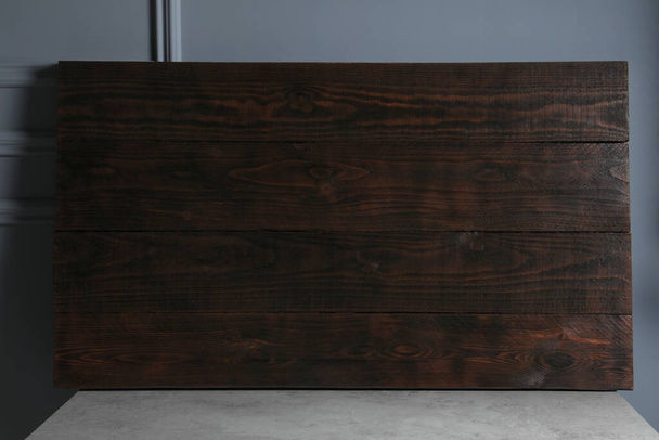 Dark wooden board on table near light grey wall - Фото, изображение