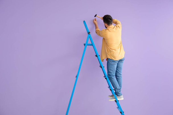 Young man with ladder nailing on lilac wall - Photo, Image