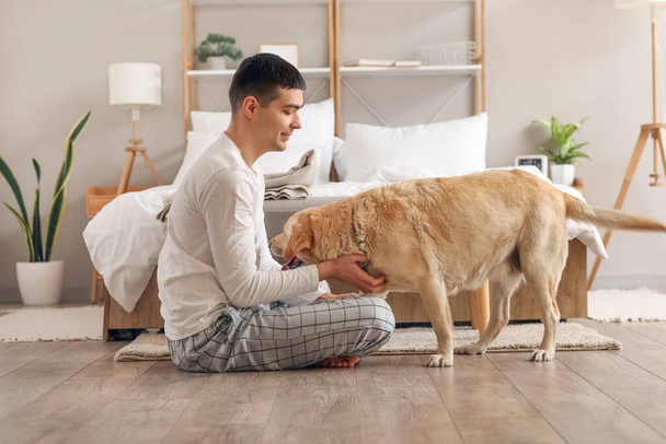 Junger Mann mit süßem Labrador-Hund im Schlafzimmer - Foto, Bild