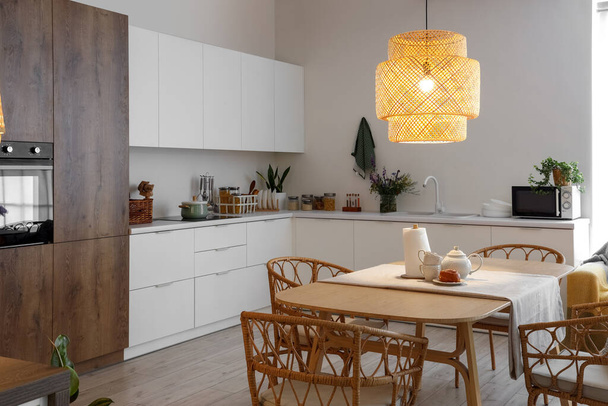 Modern mutfağın içinde, yemek masasında parlayan lamba ve çaydanlık var. - Fotoğraf, Görsel
