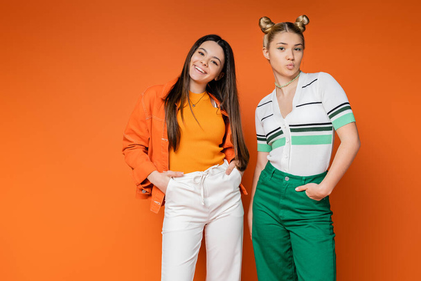 Confident and cheerful teenage girlfriends in casual outfits posing and pouting lips while looking at camera on orange background, fashionable girls with sense of style, friendship and bonding - Foto, Imagem
