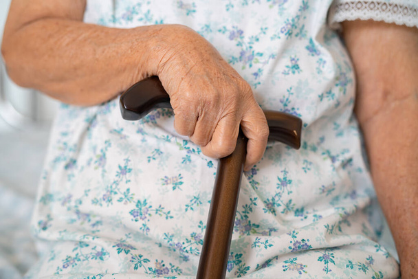 Asyalı yaşlı engelli kadın elinde baston, tahta baston, yuvarlak saplı, yürümek için yürüyen yardım.. - Fotoğraf, Görsel