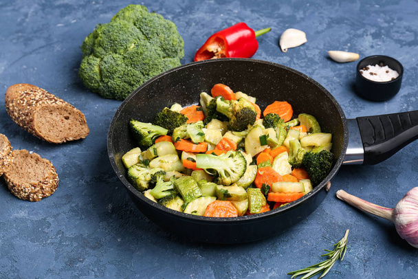 Frying pan with tasty vegetables on blue background - Photo, image
