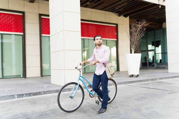 Πλήρες μήκος ενός χαρούμενου περιστασιακού επιχειρηματία στην πόλη ιππασία το ποδήλατό του και χαμογελώντας, ενώ να πάρει για να εργαστούν στο κτίριο - Φωτογραφία, εικόνα