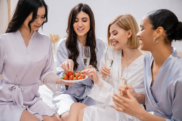 strawberries and champagne, four women, bridal party, interracial girlfriends having fun, brunette and blonde, bride and her bridesmaids spending time together, cultural diversity, bedroom  - Photo, Image
