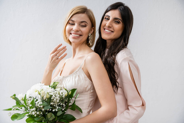 special occasion, bridesmaid hugging bride, showing engagement ring, friendship goals, grey background, happy girlfriends, bridal bouquet, blonde and brunette women, white flowers, happiness  - Photo, Image