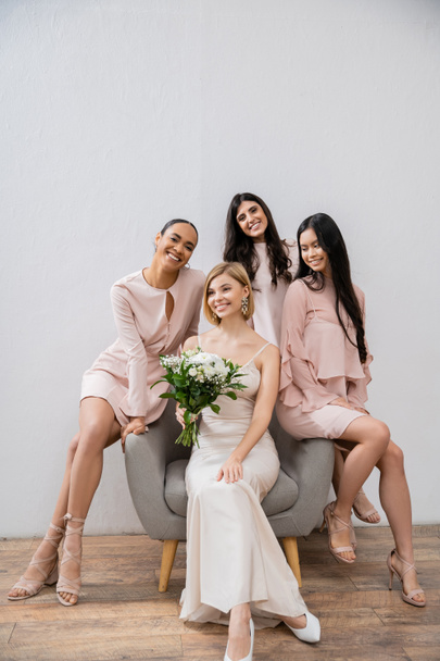 свадебная фотография, четыре женщины, подружки невесты и невесты, межрасовые подруги, день свадьбы, культурное разнообразие, сидя на кресле, серый фон, счастье и радость, свадебное платье  - Фото, изображение