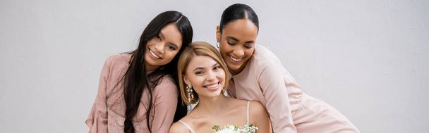 結婚式の写真文化の多様性3人の女性幸せな花嫁花束と彼女の異人種間の新婦付添人灰色の背景にアームチェアに座って、ブルネットとブロンド、喜び、お祝い、バナー  - 写真・画像