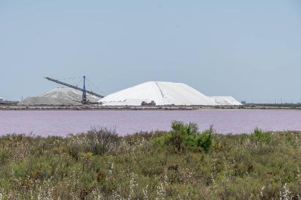Salt works, industrial plant with white piles of Camagrue sea salt and pink salty lakes, Aigues-Mortes, Gard, Occitania region of southern France - Фото, изображение