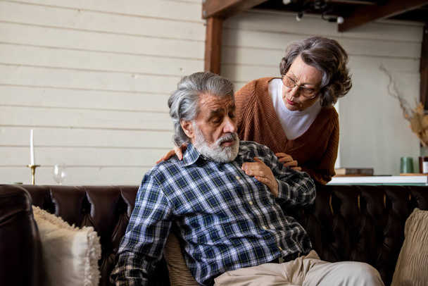 Ekose gömlekli gri saçlı bir adam kalp krizi geçirdi. Şefkatli bir eş yaşlı kocasına yardım etmeye çalışır. Yüksek kalite fotoğraf - Fotoğraf, Görsel