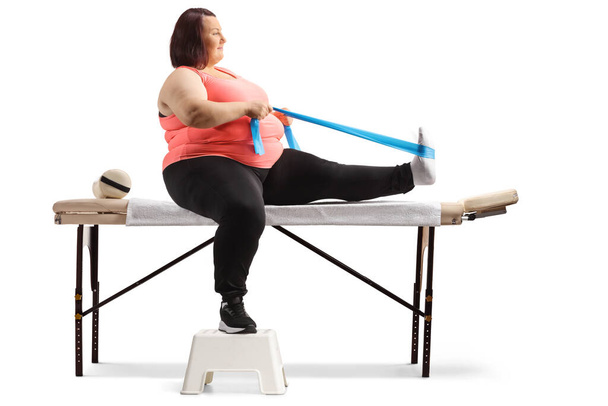 Надмірна вага жінки, сидячи на ліжку терапії і вправи з смугою опору ізольовані на білому тлі
 - Фото, зображення
