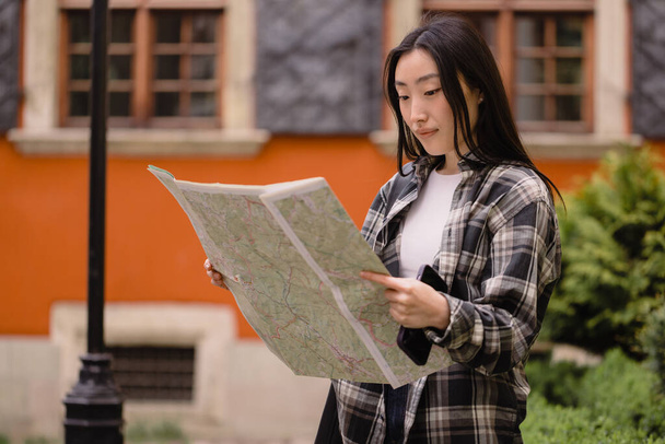 Porträt einer schönen, brünetten Koreanerin mit einer Landkarte auf den Straßen der Altstadt. Asiatische Touristin auf Reisen in Europa. - Foto, Bild