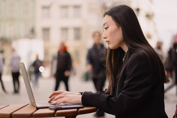 Negocios freelance joven adulto asiático mujer utilizando ordenador portátil para el trabajo y hablar por teléfono algo. Sentado al aire libre en el día. Vida urbana con tecnología moderna. - Foto, imagen