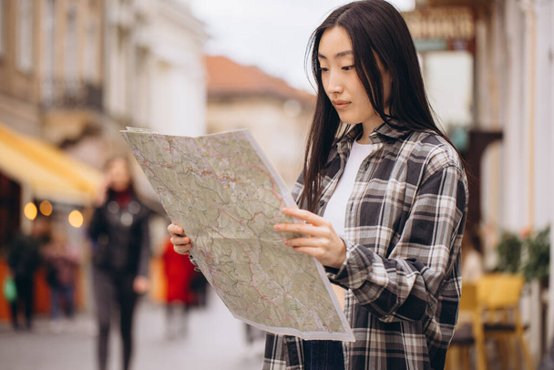 Portrait of a beautiful brunette Korean woman holding a map on the streets of the old city. Asian woman tourist or business lady traveling in Europe. - Foto, afbeelding
