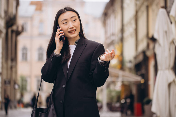 Portret pięknej Koreanki. Azjatka w luźnych ubraniach rozmawiająca przez telefon, nowoczesna technologia i styl życia. - Zdjęcie, obraz
