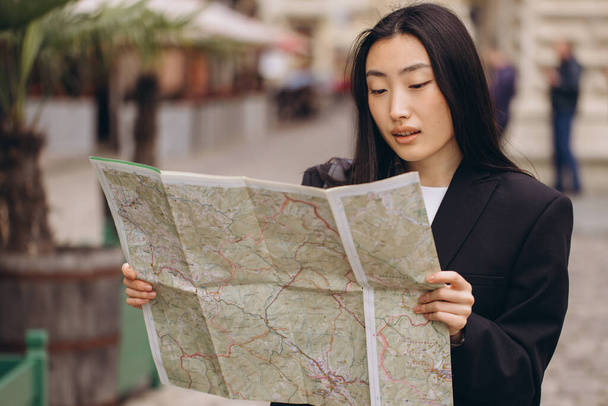 Portrait junge asiatische Touristin in lässiger Kleidung auf der Straße der alten Stadt in Europa beim Überprüfen der Richtung auf der Karte - Foto, Bild