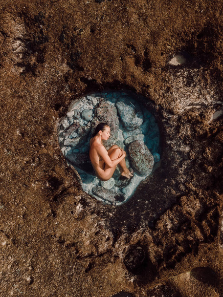 海の近くのサンゴ礁で天然プールでリラックスした裸の女性のトップの空中ビュー. - 写真・画像