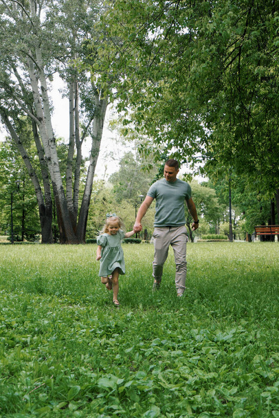 Feliz padre e hija pequeña corriendo juntos en el parque tomados de la mano Día del padre del juego familiar - Foto, imagen