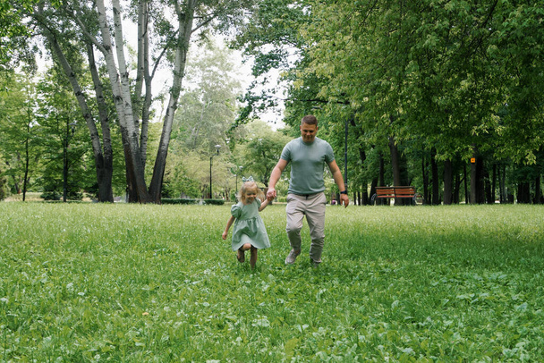 Happy father and little daughter running together in park holding hands Family game father's day - Photo, Image