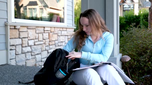 een jonge vrouw meisje neemt aktetas zitten op de veranda van het huis een rekenmachine in haar handen een telefoon in een fles water in een rugzak een trainingspak bellen een vriend op haar knieën een album map - Video