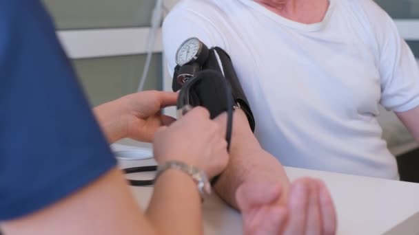 De therapeut meet de bloeddruk van een mannelijke patiënt. Bloeddruk en hartproblemen bij een oudere man. Verticale video - Video