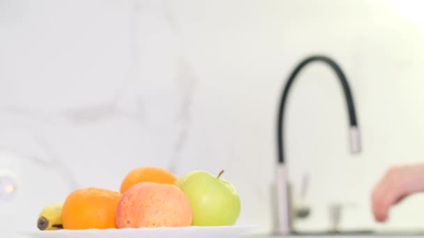 Une femme lave à la main des légumes frais sous un jet d'eau d'un robinet contre un mur blanc. Manger des aliments sains et délicieux. - Séquence, vidéo