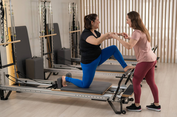 Overweight caucasian woman doing pilates exercises on reformer with personal trainer - Valokuva, kuva