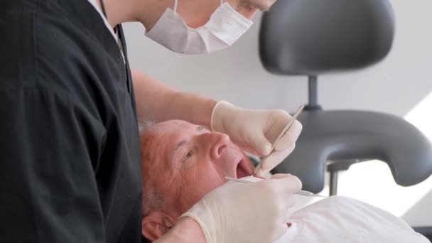 Un cirujano dental profesional en uniforme realiza una operación para instalar implantes dentales en un paciente anciano en una clínica con instrumentación moderna. 4Vídeo vertical - Metraje, vídeo