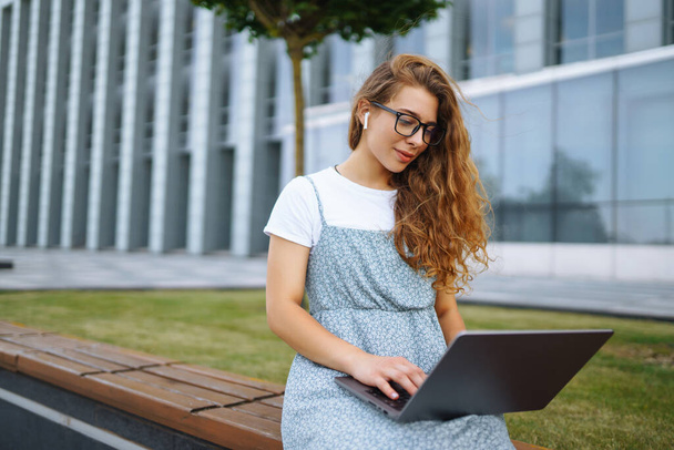Jovem mulher sentada no parque e usando laptop e digitação. Conceito de educação, online, freelance, negócios. - Foto, Imagem