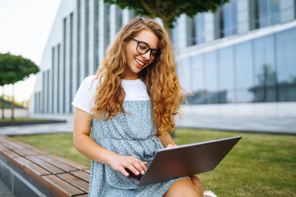 Молодая женщина, сидящая в парке и использующая ноутбук и печатающая машинки. Озил образования, онлайн, фриланса, бизнеса. - Фото, изображение