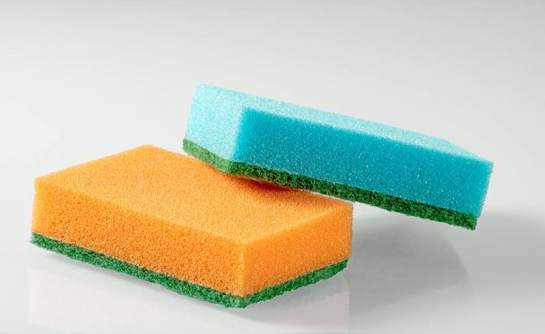 Две губки для мытья посуды оранжевым и синим цветом на белом фоне. Закрыть. - Фото, изображение