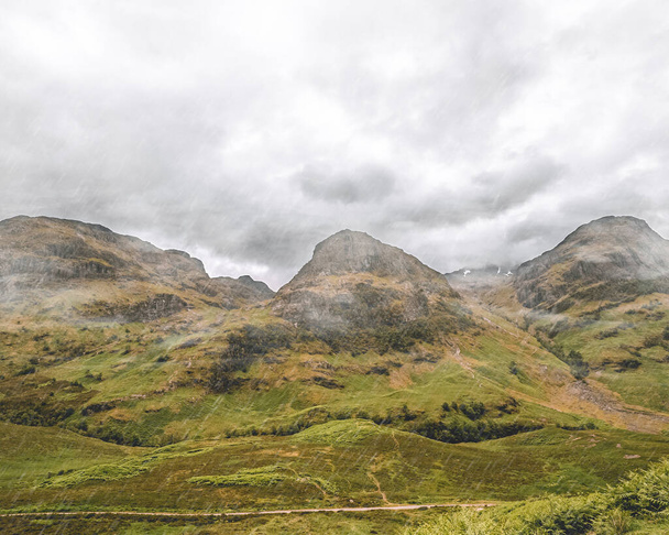 Behold the breathtaking Three Sisters view in Glencoe, Scotland. Towering mountains form a magnificent backdrop, their peaks shrouded in mist. The rugged beauty of the landscape captivates, as the grandeur of nature unfolds, leaving visitors in awe o - Foto, afbeelding