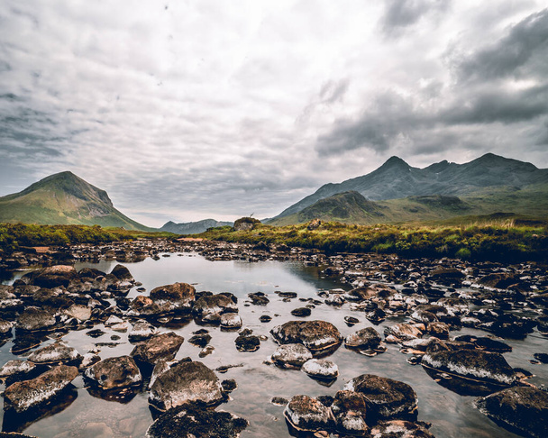 A panoramic vista unfolds, revealing the majestic mountain peaks of the Scottish Highlands. As far as the eye can see, rugged summits pierce the sky, adorned with sweeping slopes and veils of mist. This awe-inspiring landscape encapsulates the untame - Foto, afbeelding