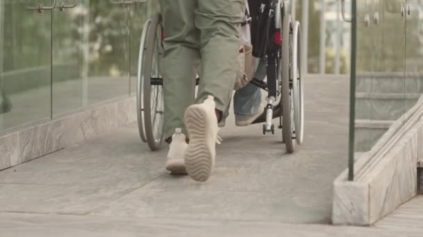 Взгляд сзади: неузнаваемый мужчина помогает инвалиду-колясочнику взобраться на небольшую высотку в городе - Кадры, видео