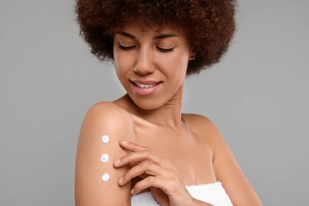 Beautiful young woman applying body cream onto arm on grey background - Photo, image