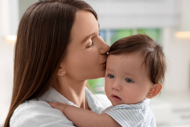 Щаслива мати цілує свою маленьку дитину в приміщенні, крупним планом
 - Фото, зображення