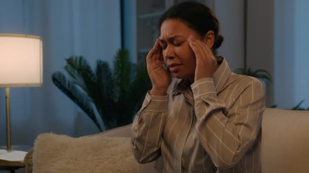 Zieke Afro-Amerikaanse vrouw gebruik mobiele telefoon gadget verslaafde 's avonds thuis ziek ongezond meisje op de bank voelen hoofdpijn migraine pijnlijke hoofd kramp masseren tempels pijn hoge bloeddruk - Video