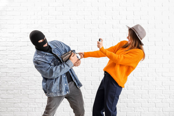 Young woman with pepper spray defending herself against thief on white brick background - Foto, Imagen