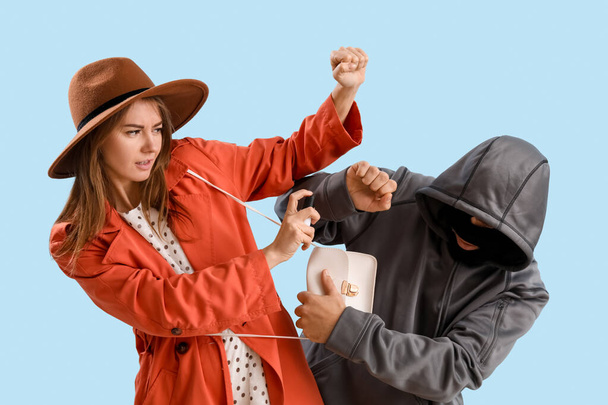 Young woman with pepper spray defending herself against thief on blue background - Fotoğraf, Görsel